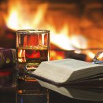 Glass alcoholic drink wine antique books in front warm fireplace.
