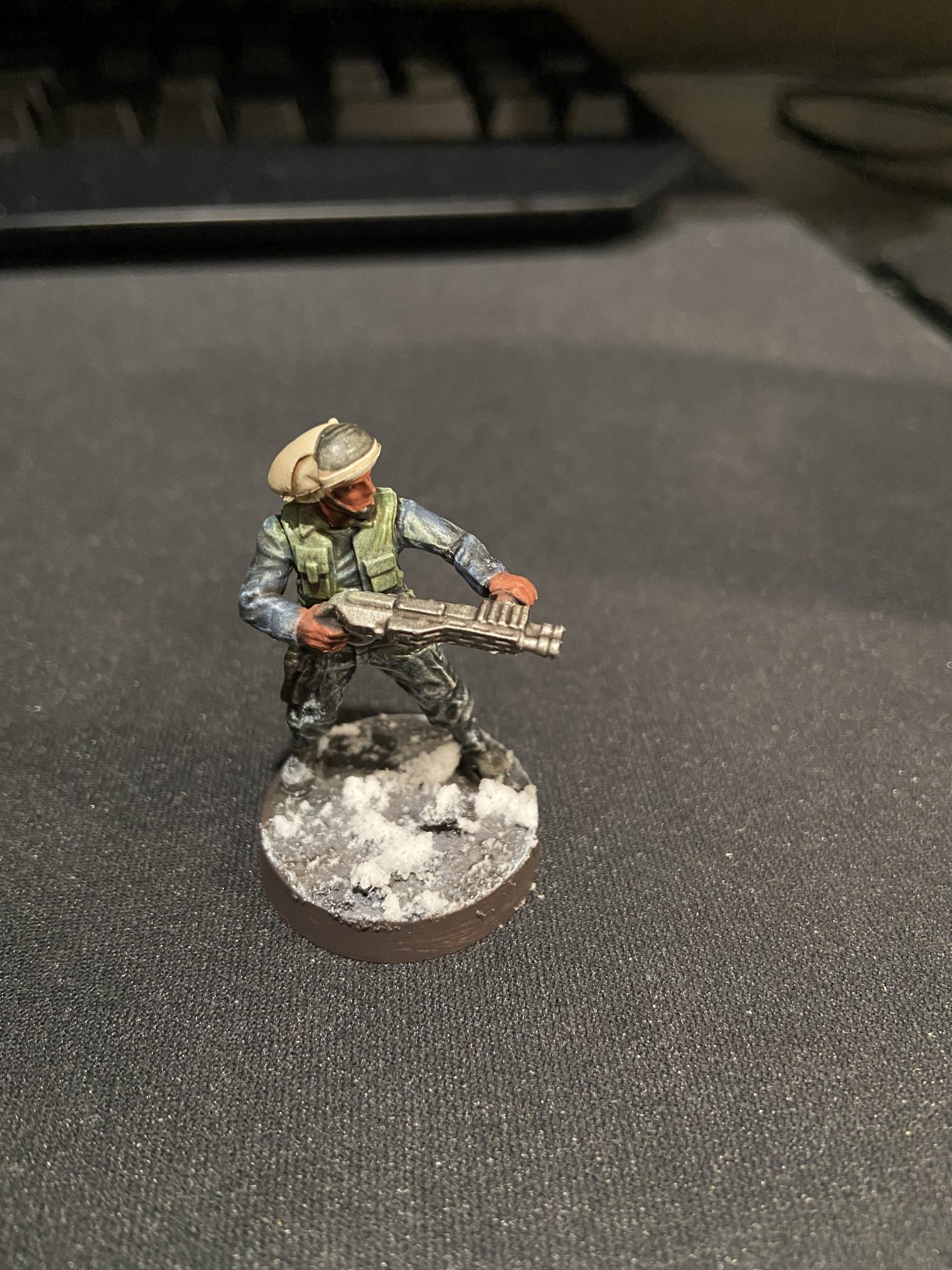 A Star Wars Legion Rebel with a green jacket and blue under layer, the base is covered in snow. Credit Jon.Kil