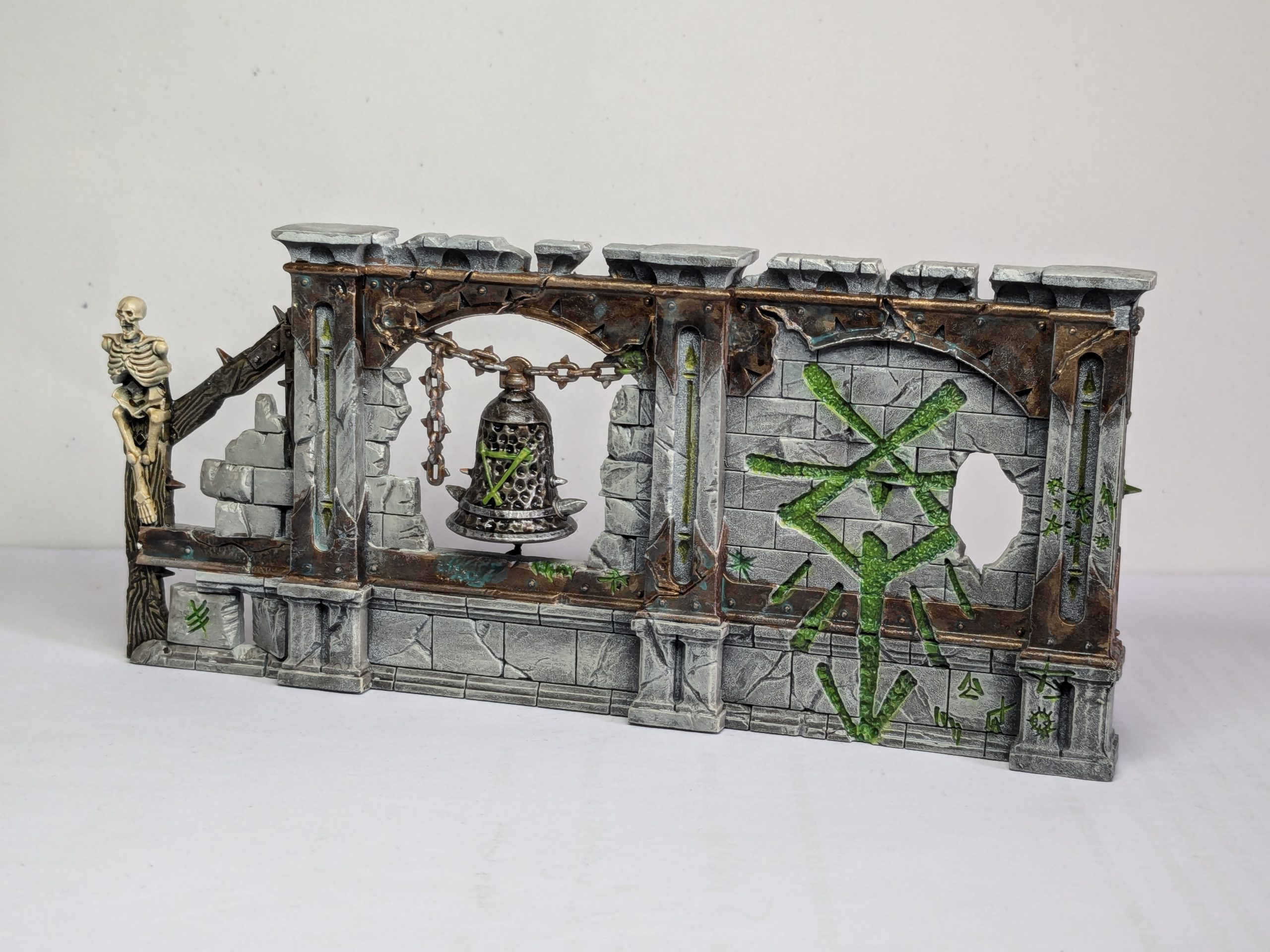 Terrain from Spearhead: Fire and Jade, featuring Skaven graffiti and a brass bell. Credit: Roxin